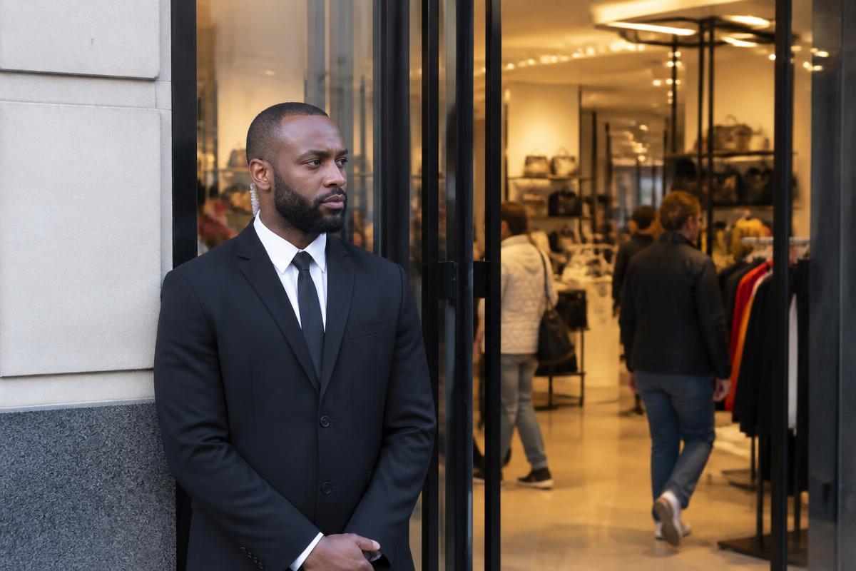 Agent de sécurité en costume sombre surveillant l'entrée d'un magasin en journée